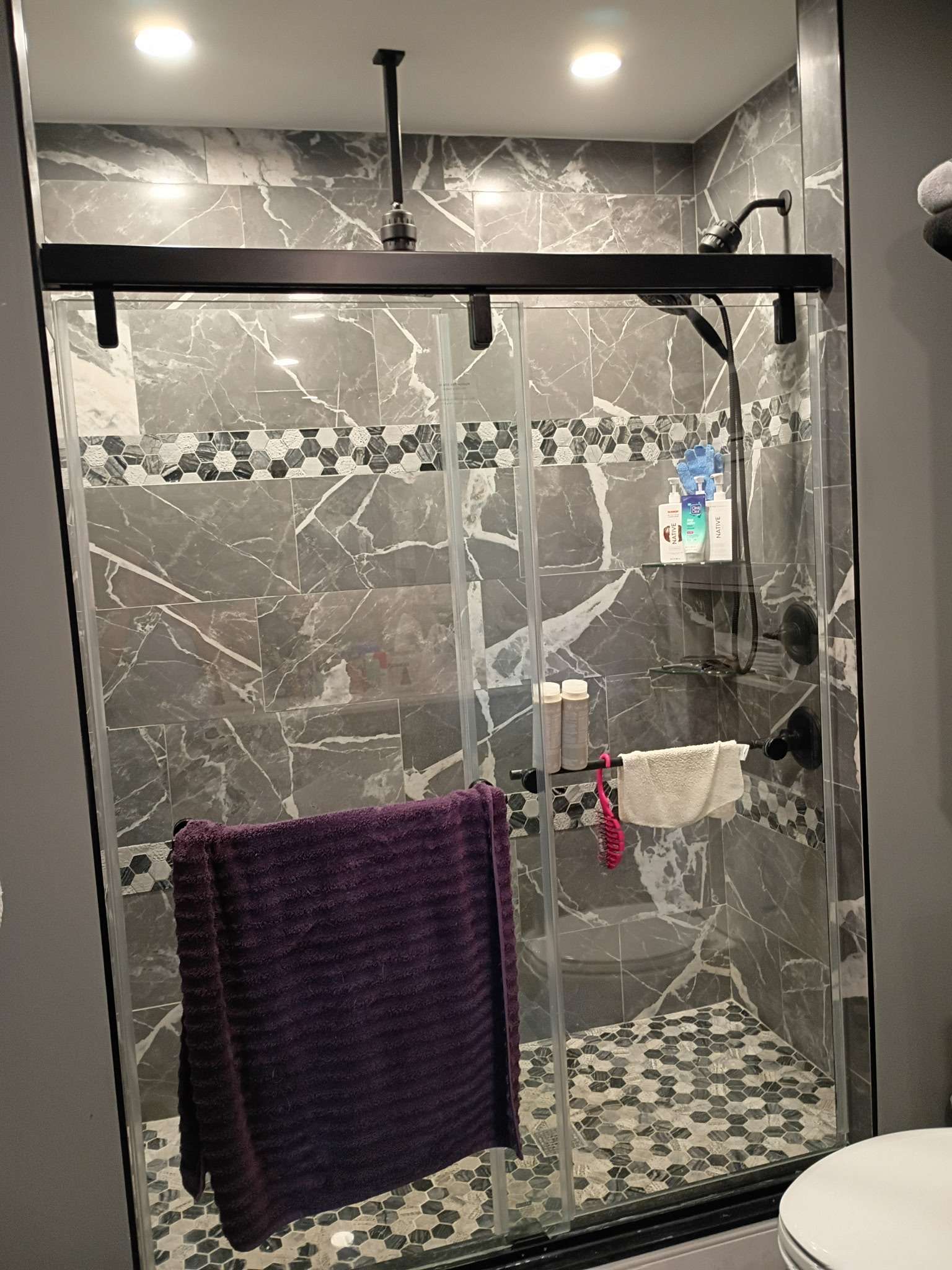 Remodeled shower with gray marble tile, hex mosaic accents, and a glass sliding door by Handy Handyman Services